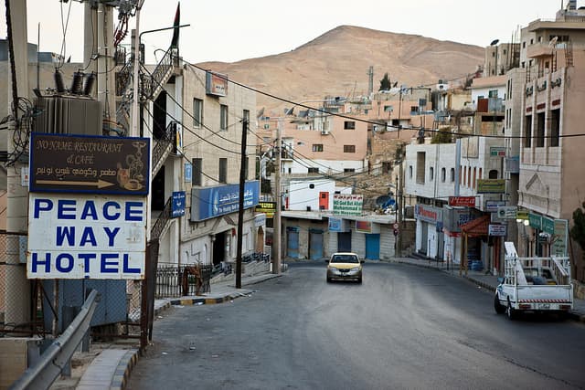 Test image: a hillside town street with a Peace Way Hotel sign, a No Name Restaurant and Cafe sign in English and Arabic, a car, and a truck